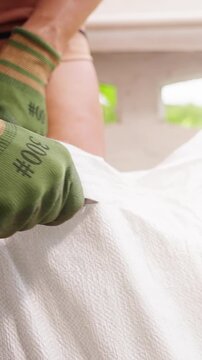 Vertical video. Woman Wearing Protective Gloves Cuts Open a Sealed White Soil Bag with a Knife, Solving a Packaging Problem during Gardening Preparation