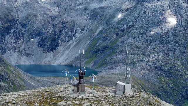 Aerial view of the monitoring station with wind turbines and sensors on a rocky peak overlooking a small alpine lake in the Trollstigen area, Andalsnes, More og Romsdal, Norway.