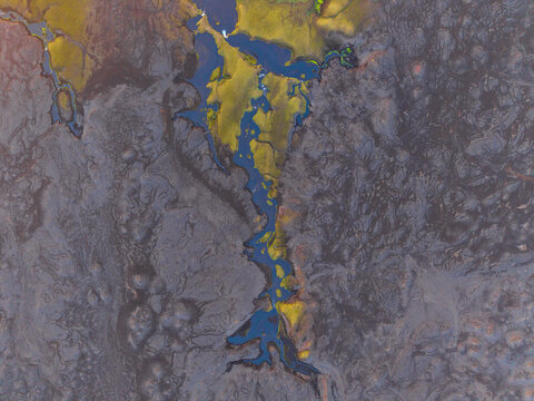 Aerial view of a winding river cutting through a dark volcanic lava field with vibrant green mossy banks in Iceland.