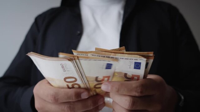 Close-up of a person holding and counting a large stack of fifty euro banknotes indoors, representing income, savings, salary, wealth and personal financial management.