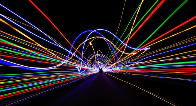A long tunnel is illuminated by a series of colorful light trails. The streaks of light create a dynamic and abstract pattern, suggesting movement and speed.