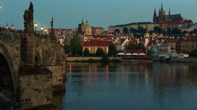 Historic Charles Bridge spans the Vltava River in Prague during early morning dawn. Saint Vitus Cathedral and Prague Castle dominate the European city skyline. Classic urban travel view.