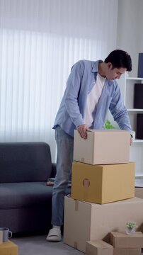 Young Asian man sealing cardboard box with packing tape in modern apartment during home relocation