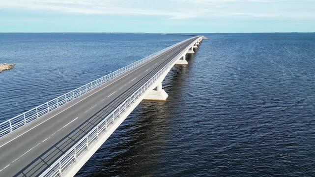 Aerial view of the long Riutunkari causeway bridge crossing the sea with a red car driving along the road in Oulu, North Ostrobothnia, Finland.