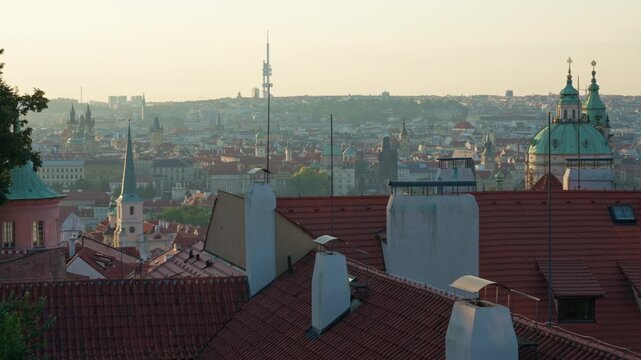 Prague city skyline features historic church domes and famous spires at dawn. Warm morning light illuminates traditional Czech architecture. European travel scene showcases urban heritage.