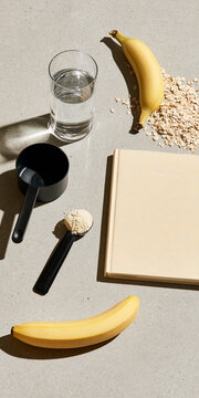 A flat lay of ingredients for a healthy shake: banana, oats, protein powder, a glass of water and a recipe book