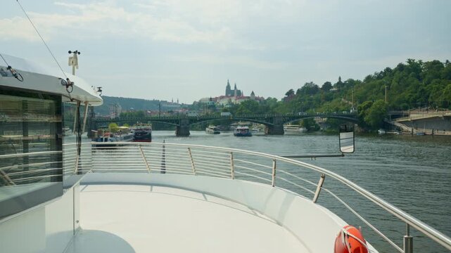 A tourist cruise boat sails along the Vltava River in Prague. Historic bridges and Prague Castle decorate the scenic urban skyline. Passengers enjoy sightseeing during a relaxing vacation.