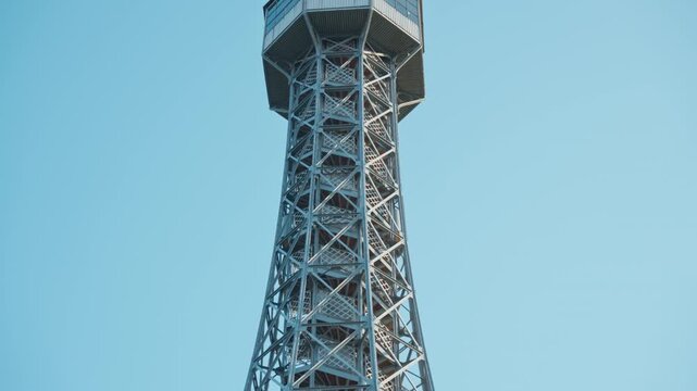 Petrin Lookout Tower features a steel lattice structure in Prague, Czechia. Historic architectural landmark offers observation decks for European tourism. Metal framework stands against blue sky.