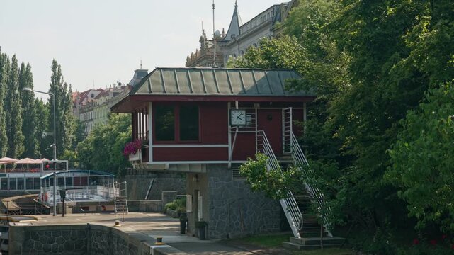 Smichov Lock control house stands along Vltava River in Prague, Czechia. Historic operator building with exterior stairs manages canal navigation. European waterway infrastructure scene.