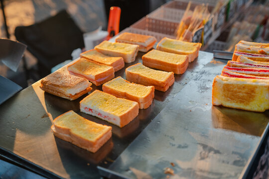 Slices of golden buttered toasted bread lined up on flat hot grill.