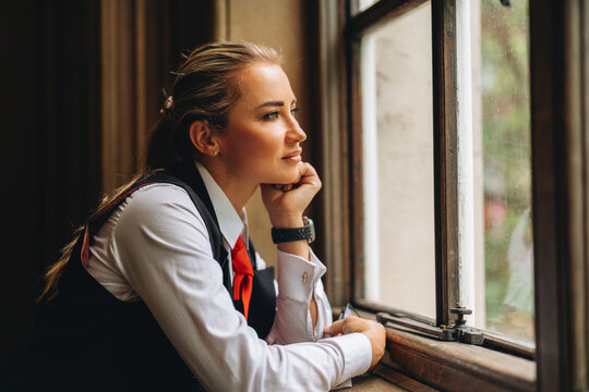 Woman looks out of a window while resting her chin on her hand in an indoor setting during daytime