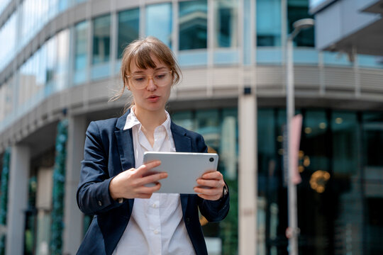 Businesswoman uses tablet while standing in front of a glass building in a city during daytime