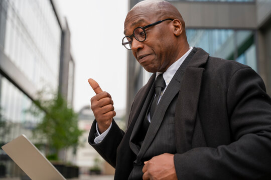 Business person gives a thumbs up while using a laptop outside in a city area during the day
