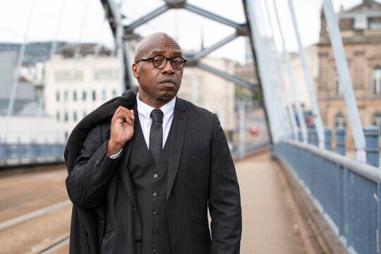 Man walking on bridge in city while holding jacket over shoulder during daytime