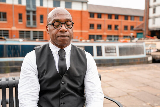 Man sits quietly on a bench near boats in a waterfront area during the day in an urban setting