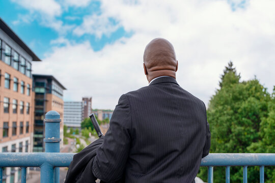 Man looking at city buildings while holding a phone and wearing a suit on a balcony in an urban area