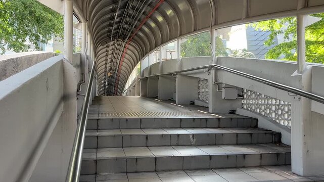 Daily commuters walking through modern pedestrian link bridge at KTM railway station in Kuala Lumpur city center.