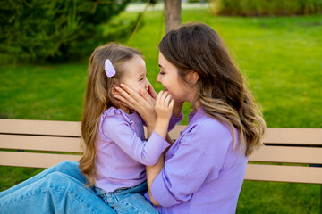 Fototapeta premium mother and child walking in the park in the summer, having fun together, mother and daughter hugging and kissing on a green lawn, motherly love