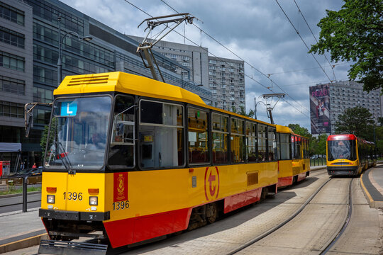 Warsaw, Masovian Voivodeship, Poland - July 08 2026: A classic yellow and red public tram moves along city rails surrounded by modern urban buildings under a cloudy sky.