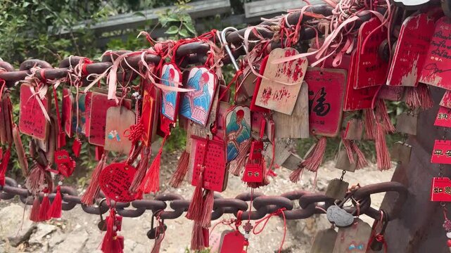 Many wooden prayer plaques hang from a rusty metal chain at a sacred site. Traditional temple wish tablets with red tassels for luck, faith, and religious rite.