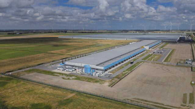 Aerial view of Google data center Agriport A7 surrounded by agricultural fields and wind turbines under a cloudy sky in Middenmeer, North Holland, Netherlands.