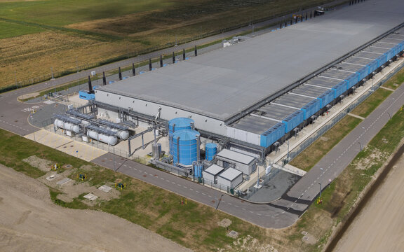 Aerial view of the Google data center Agriport A7 featuring large industrial buildings, blue cooling tanks, and surrounding agricultural fields in Middenmeer, North Holland, Netherlands.