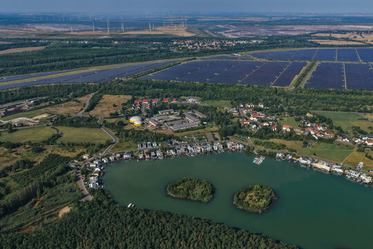 Aerial view of the recultivated coal mines Leipziger Neuseenland featuring a lake with islands, residential houses along the shore, and a large solar park in Kahnsdorf, Saxony, Germany.