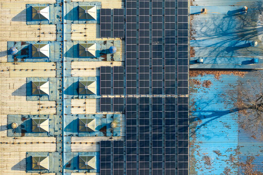 Aerial view of rooftop solar panels installed on an industrial building, generating renewable energy with skylights and blue metal roofing in Zemun, Vojvodina, Serbia.