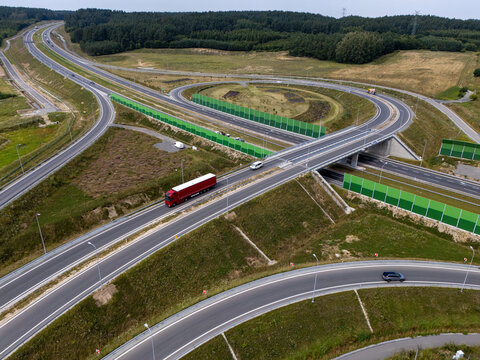 Aerial view of a highway interchange with a red truck driving on the road, surrounded by green noise barriers and grassy embankments in Gdansk, Poland.