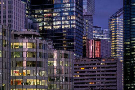 Evening settles over La Defense, Paris, where glass office buildings layer windows and lights across a skyline shaped by concentrated urban density.