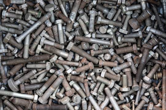 Background old rusty mixed metal bolts and screws. Pile various vintage steel bolts, screws and fasteners. Concept of construction waste, scrap metal recycling, old workshop hardware and mechanics