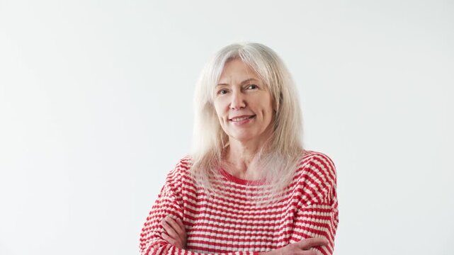 Friendly senior Caucasian woman standing with crossed arms and smiling at camera. Mature female showing confidence warmth and positive attitude against clean background. Lifestyle portrait.