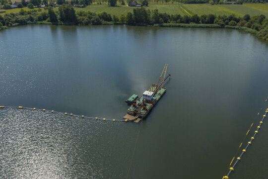 Aerial view of a dredging vessel operating in a lake with floating pipes and buoys, surrounded by green fields and trees, Zwolle, Netherlands.