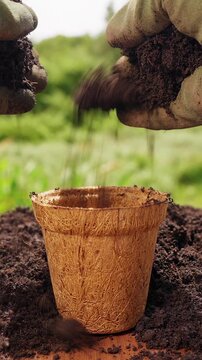 Vertical video. Hands in Gardening Gloves Cover a Planted Seed With Soil Inside a Coconut Fiber Pot Outdoors, Germination, New Life and Sustainable Cultivation