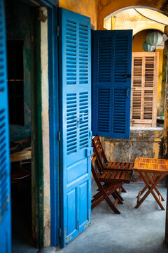 Vintage blue colored wooden doors and table with chairs setting in traditional cafe in Hoi An, Vietnam, authentic exterior of Vietnamese cafe with old wooden doors and window shutters in ancient style