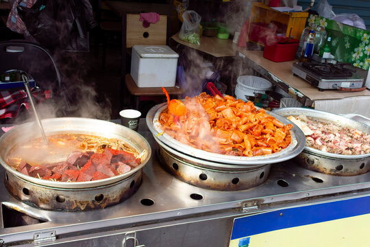 A Korean street food stall in Busan offers a variety of dishes steaming in large metal pans