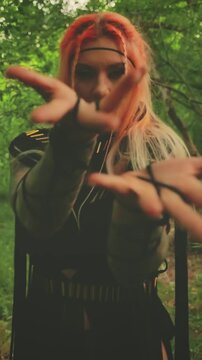Halloween holiday woman witch conjuring with hands, dancing looking at camera walking in dark forest green tree. long black dress gothic boho style macrame, elf fairy girl shaman. vertical video crop.