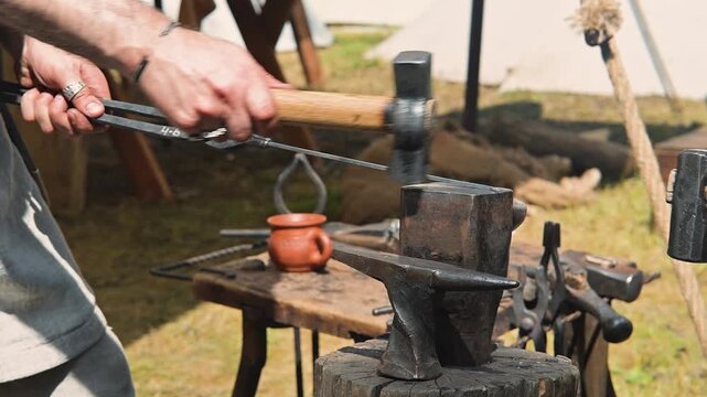 A blacksmith shapes metal on an anvil using a hammer, demonstrating traditional crafting techniques in a medieval setting