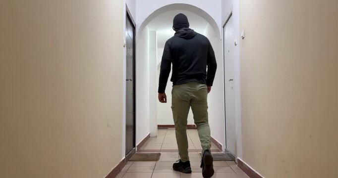 Masked burglar breaking into apartment door in residential building hallway - home burglary crime concept