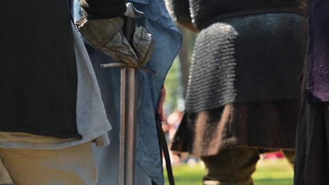 Men in dark clothing with chainmail armor prepare tools and weapons before a battle in a wooded area. The atmosphere reflects the early Middle Ages, highlighting the urgency of the moment