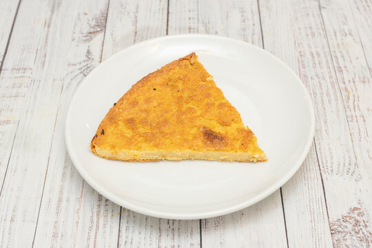Golden triangular slice of baked chickpea flour fain&aacute;, served on white plate over weathered wooden table
