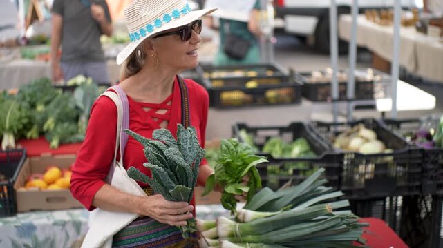 Mature woman smiles as she selects vegetables and fruits at the Farmers Market in Sonoma, California on a sunny morning.