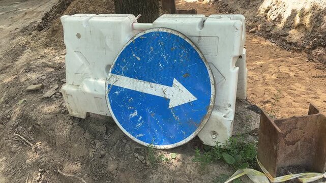 Round blue detour sign with a white directional arrow in a roadwork zone, traffic control, construction safety, urban navigation.