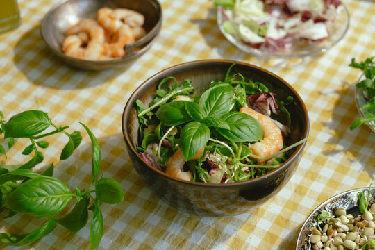 Seasonal summer salad with shrimps garnished with fresh basil leaves on yellow white tablecloth. Heathy dinner. Mediterranean kitchen. 