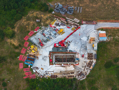 Aerial view of a construction site with a red mobile crane near a concrete foundation and various building materials scattered around in Serravalle Scrivia, Piedmont, Italy.
