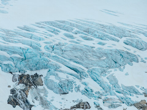 Aerial view of a glacier with deep blue crevasses and melting ice flowing over rocky terrain in Valldal, More og Romsdal, Norway.
