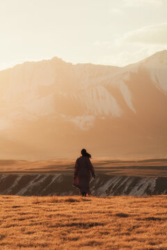 Asian Woman Standing in Golden Steppe Landscape with Snowy Mountain Range at Sary Jaz Valley