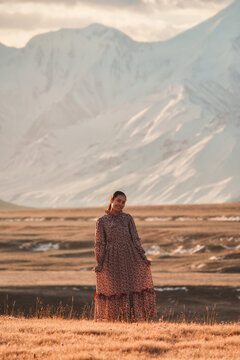 Asian Woman Standing in Golden Steppe Landscape with Snowy Mountain Range at Sary Jaz Valley