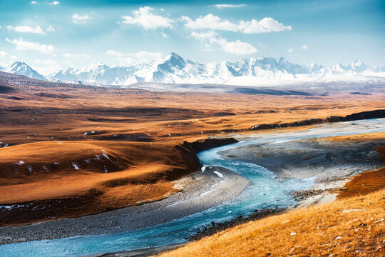Turquoise Glacial River Flowing Through Golden Steppe and Snow Capped Mountain Range in Central Asia