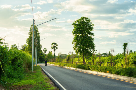 Motorcyclist Riding Rural Road Through Lush Green Tropical Landscape in Countryside Thailand